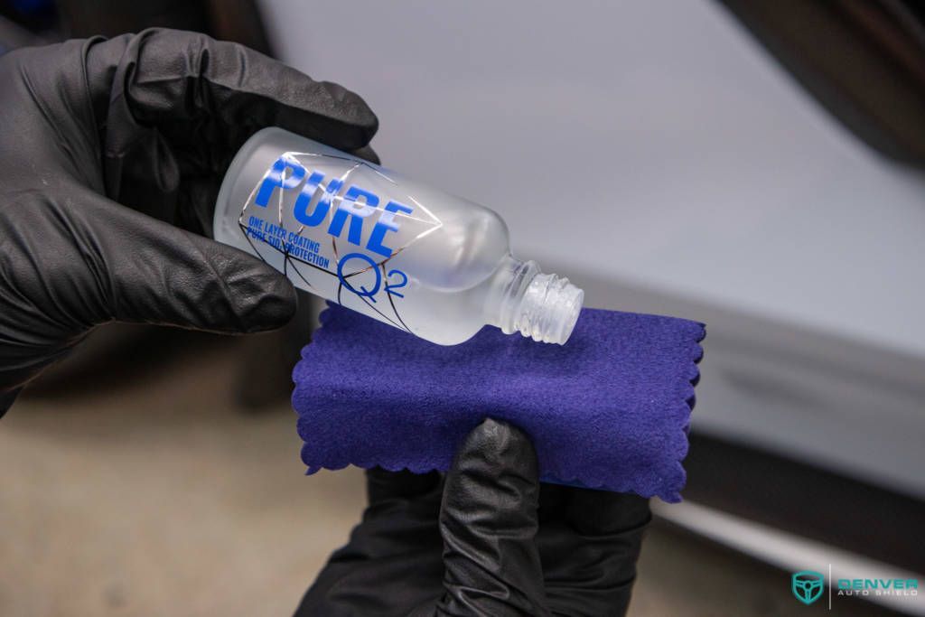 A person is holding a bottle of ceramic coating on a purple cloth.