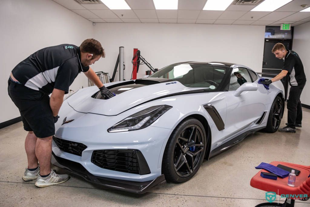 Two men are cleaning a white sports car in a garage.