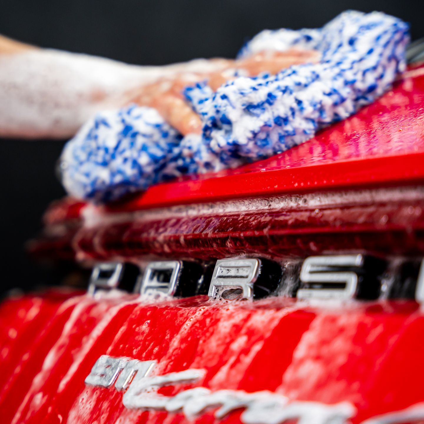 A person is washing a red car with a towel.