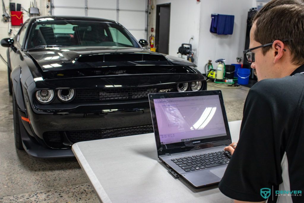 A man is using a laptop in front of a black car.