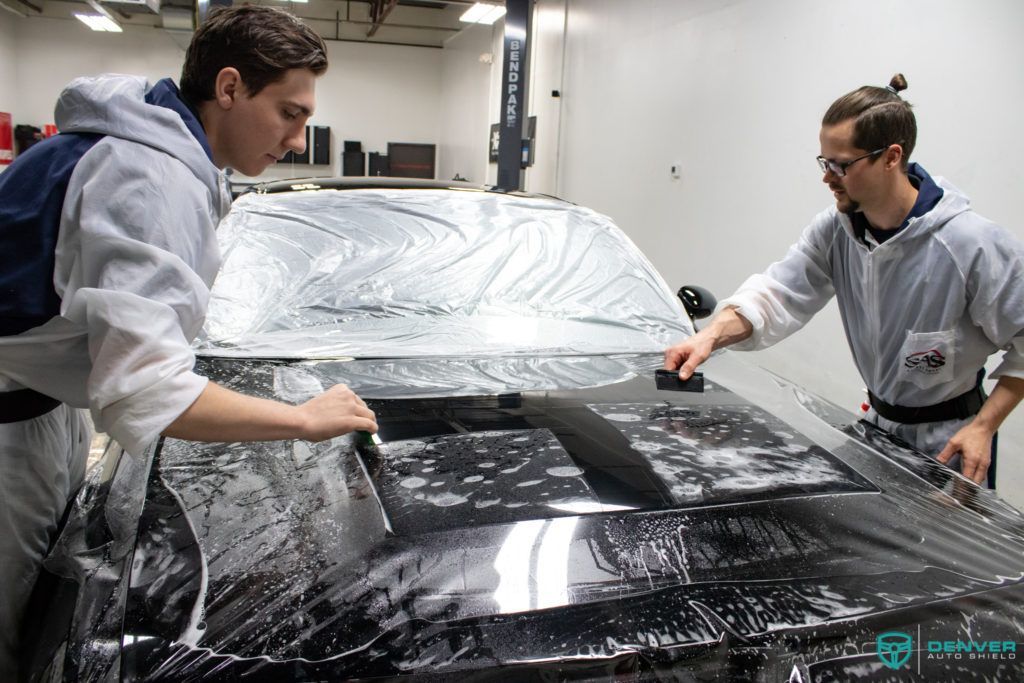 Two men are wrapping a car in plastic in a garage.