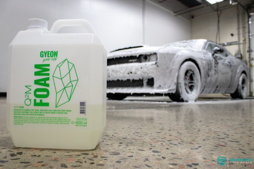 A bottle of foam next to a car covered in foam.