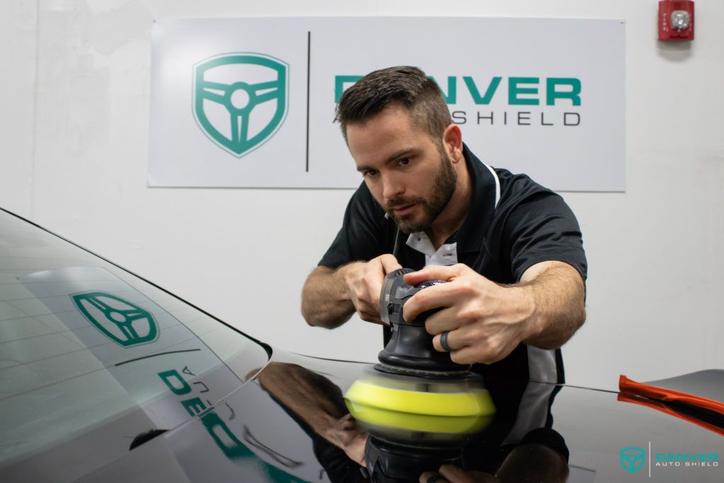 A man is polishing a car windshield with a machine.