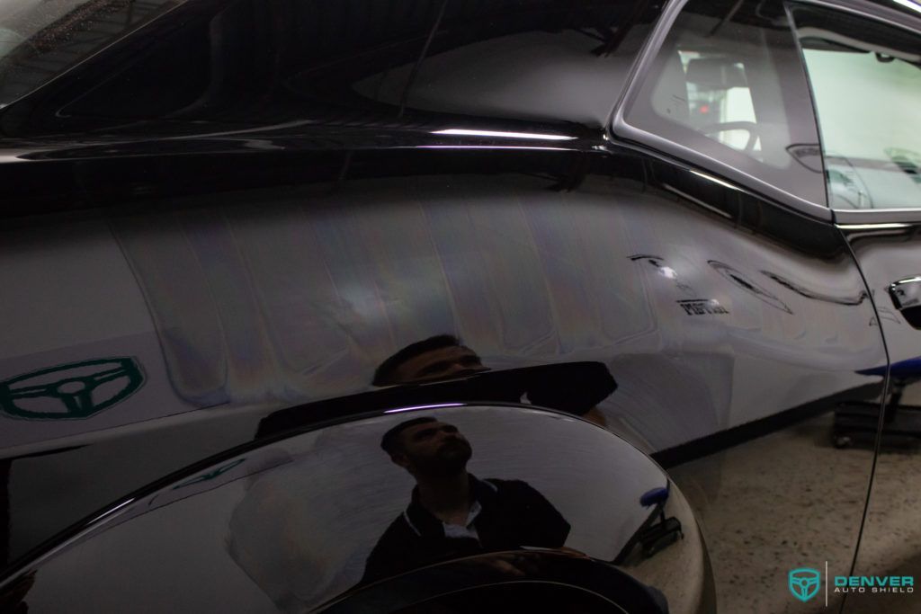 A man is reflected in the fender of a black car.