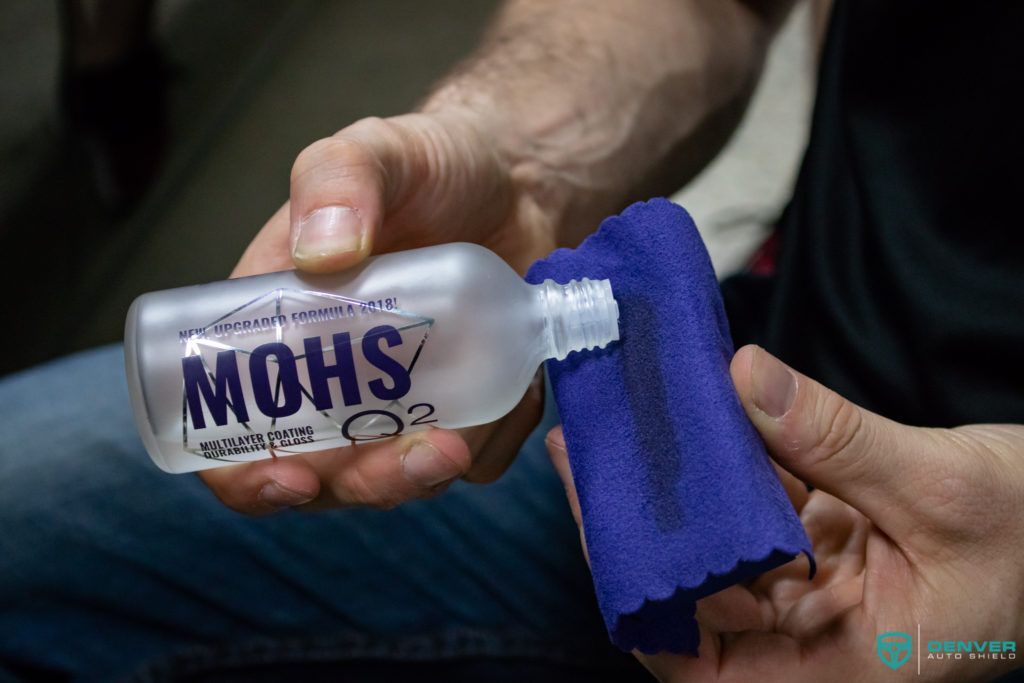 A person is holding a bottle of mohs and a blue cloth.