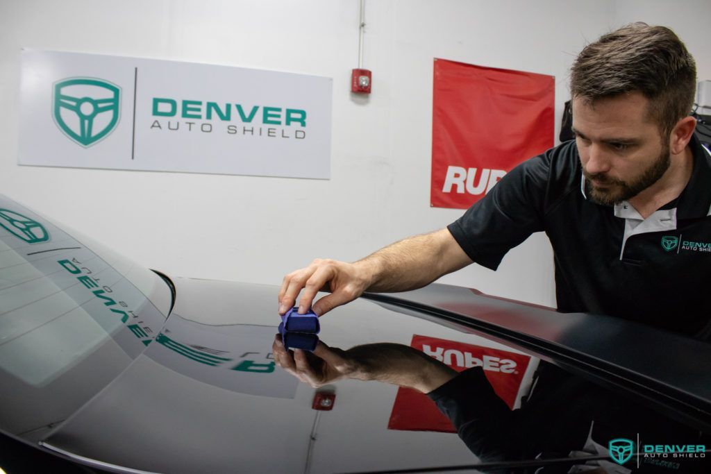 A man is polishing the windshield of a car in a garage.