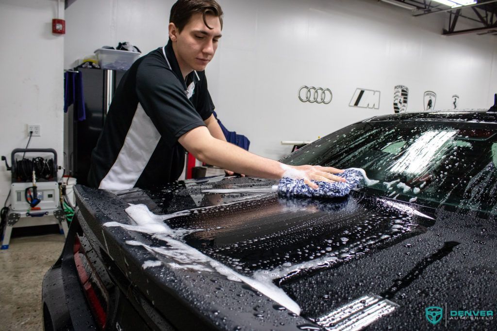 A man is washing a car with a cloth in a garage.