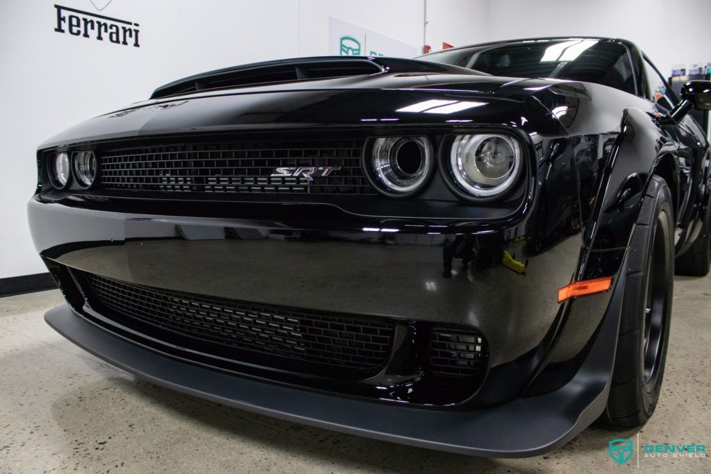 A black dodge challenger demon is parked in a ferrari showroom.