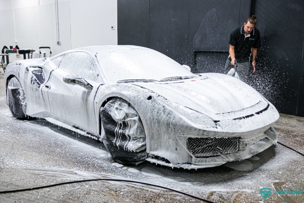 A man is washing a ferrari with foam in a garage.