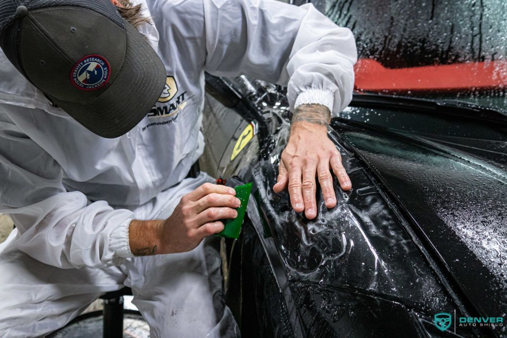 A man in a white suit is cleaning a car with a green brush.