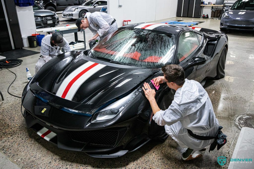 Two men are cleaning a black sports car in a garage.