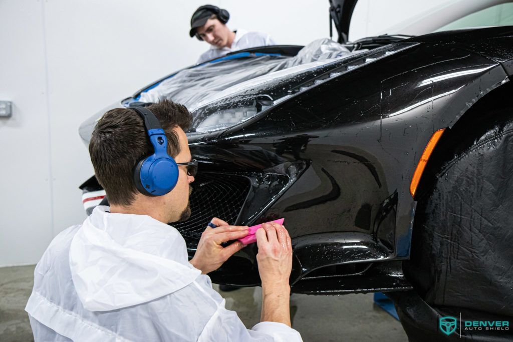 A man wearing headphones is working on a black car.