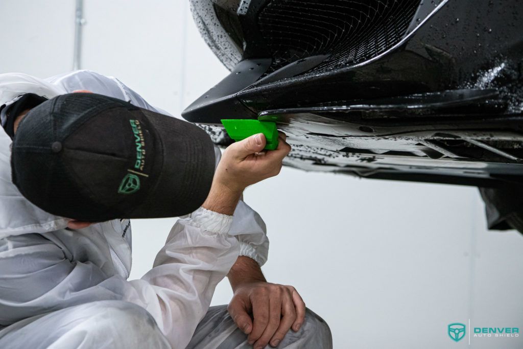 A man is kneeling down and cleaning the underside of a car.