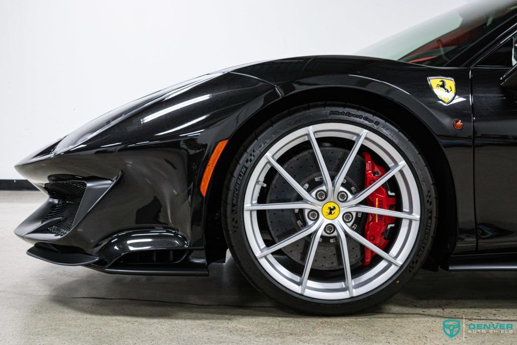 A black ferrari with red brake calipers is parked in a garage.