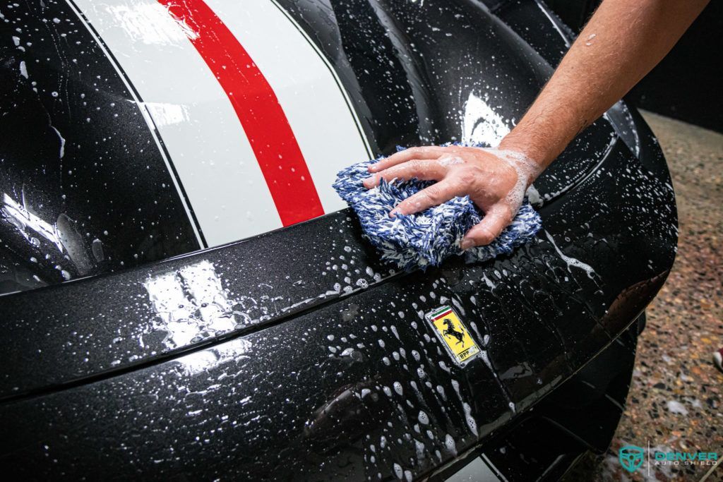 A person is washing a black car with a towel.