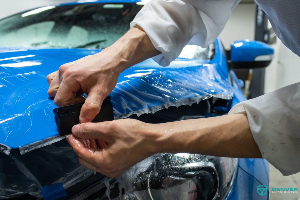 A man is wrapping a blue car with a protective film.