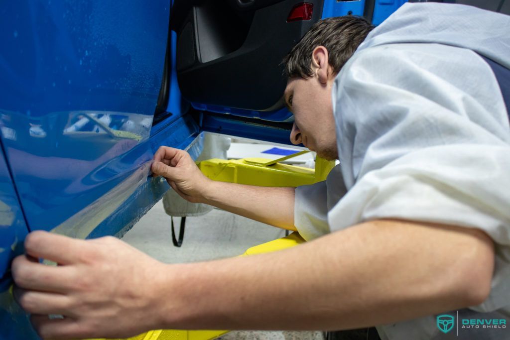 A man in a white shirt is working on a blue car.