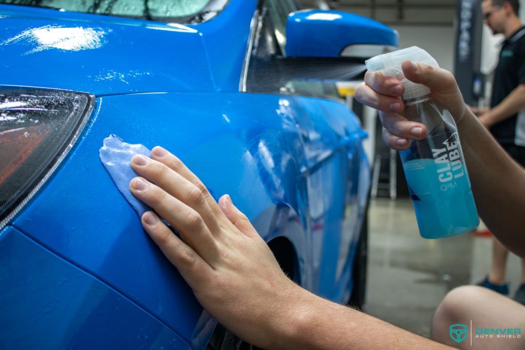 A person is cleaning a blue car with a spray bottle.