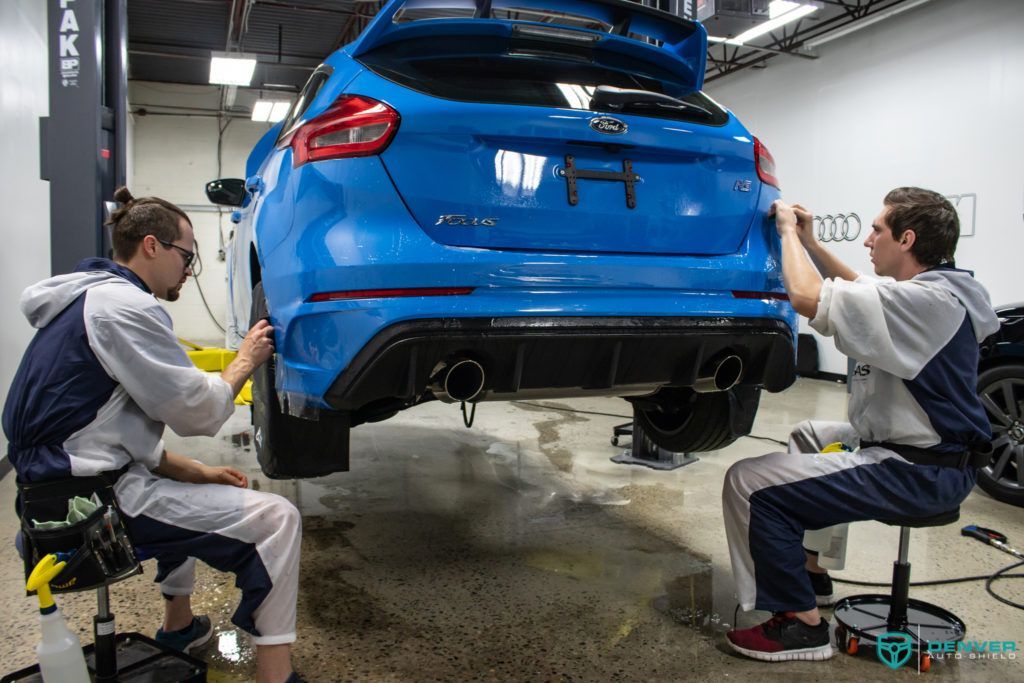 Two men are working on a blue car in a garage.