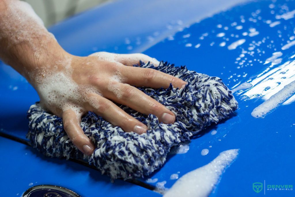 A person is washing a blue car with a sponge.