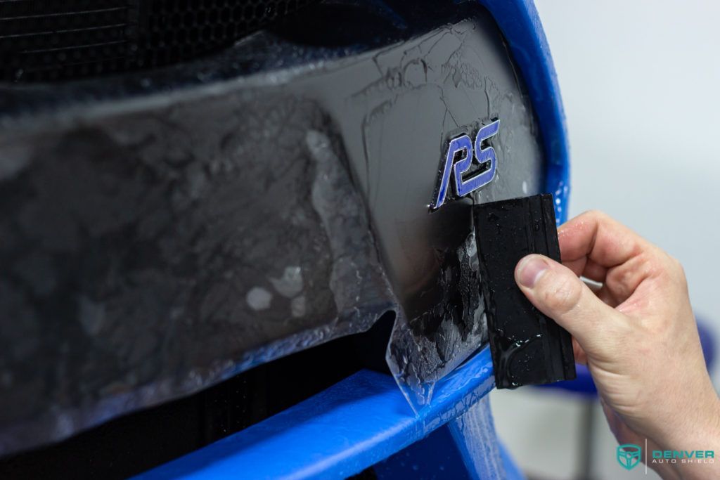 A person is holding a piece of tape over a blue car.