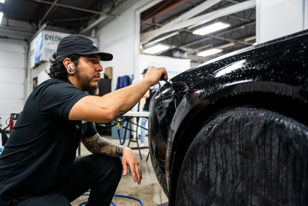 A man is kneeling down in front of a black car.