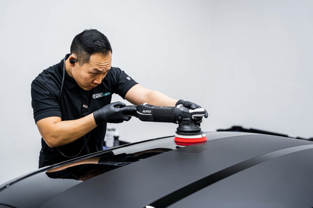 A man is polishing the roof of a black car with a machine.