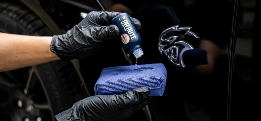 A person wearing black gloves is applying a coating to a car.