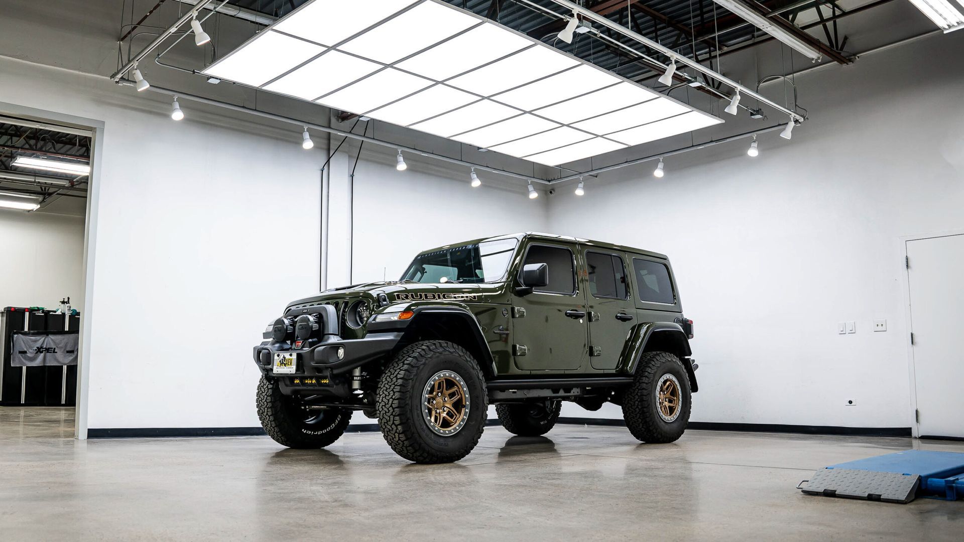 A green jeep is parked in a garage under a ceiling light.