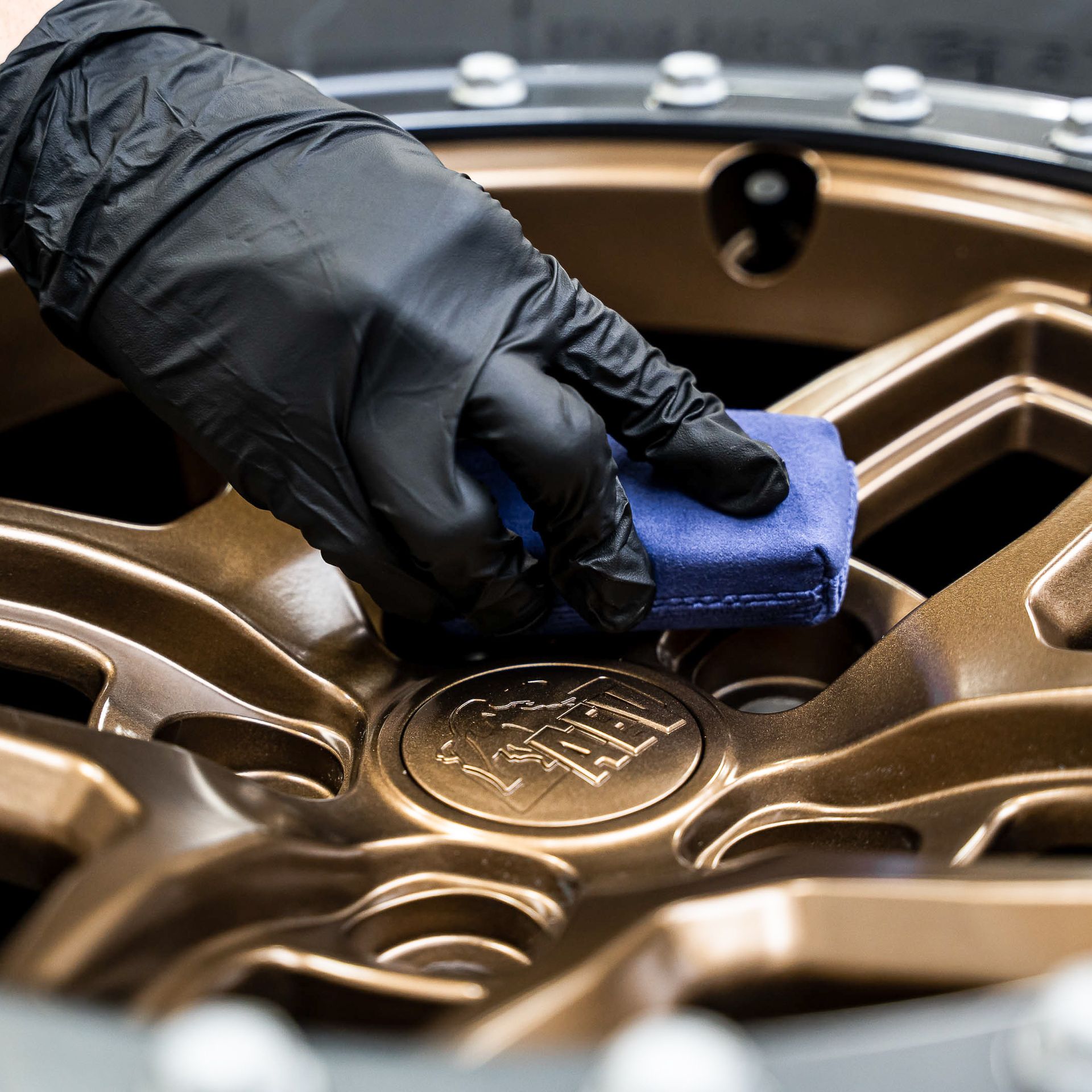 A person wearing black gloves is cleaning a wheel with a blue sponge.