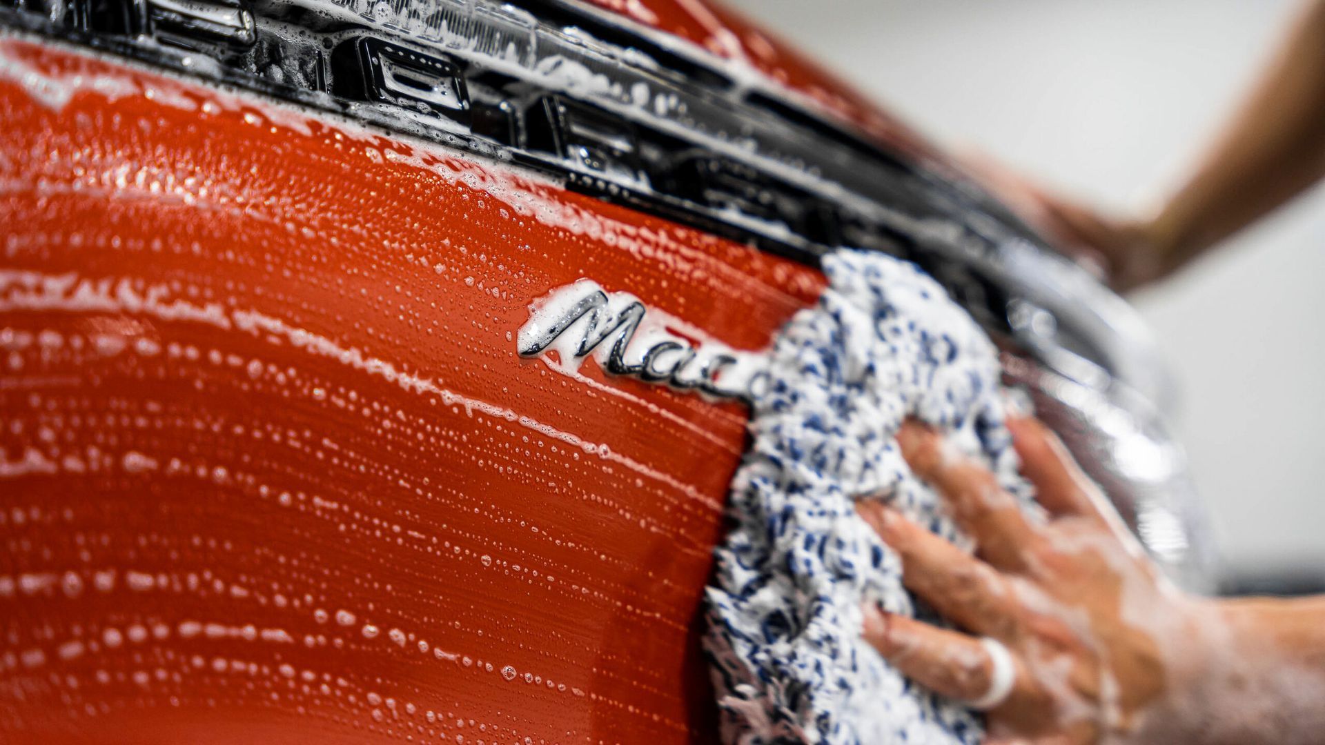 A person is washing a red car with a towel.