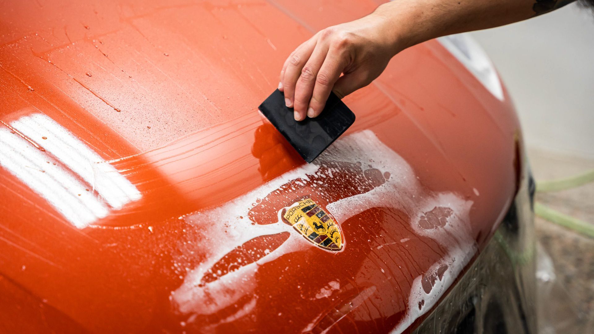 A person is cleaning the hood of a car with a sponge.