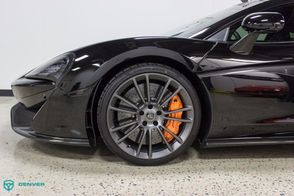 A black sports car with orange brake calipers is parked in a garage.