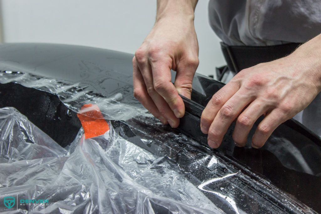 A man is covering a car with plastic wrap.