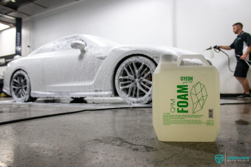 A man is washing a car with foam next to a bottle of foam.