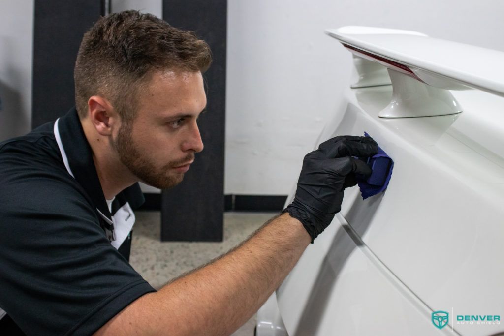 A man wearing black gloves is cleaning a white car.