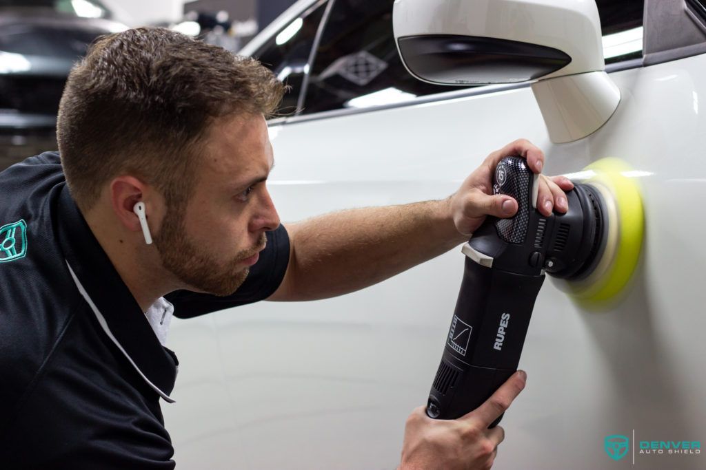 A man is polishing a white car with a machine.