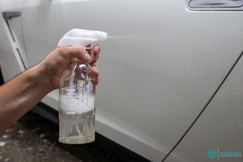 A person is holding a spray bottle in front of a white car.