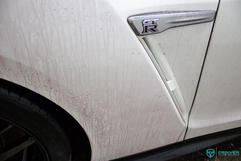 A close up of a white car with a dirty fender.