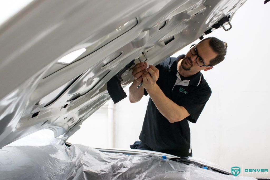 A man is working on the hood of a car.