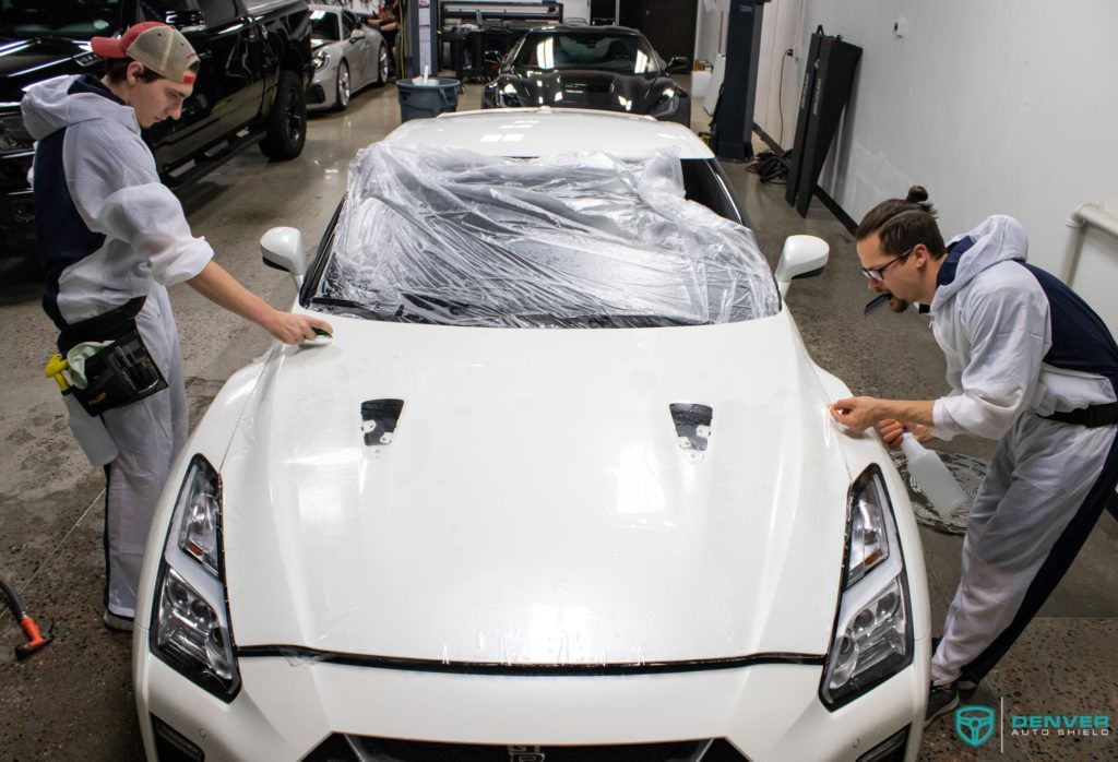 Two men are working on a white car in a garage.