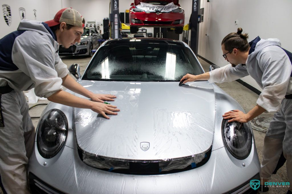 Two men are polishing a silver car in a garage.