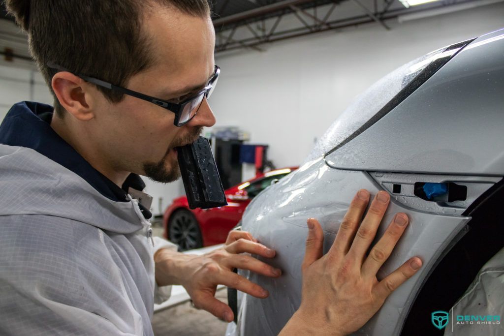 A man is applying a protective film to the side of a car.