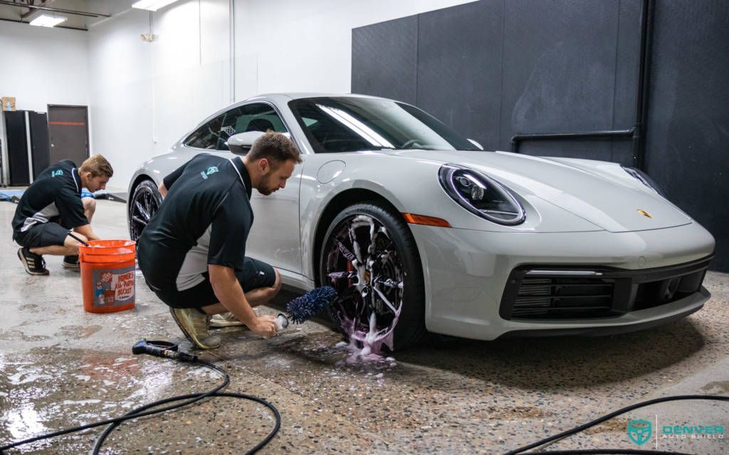 Two men are washing a white porsche 911 in a garage.