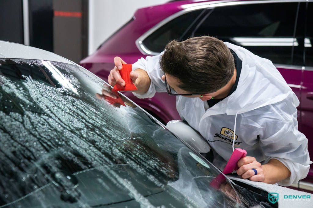 A man is cleaning the windshield of a purple car.