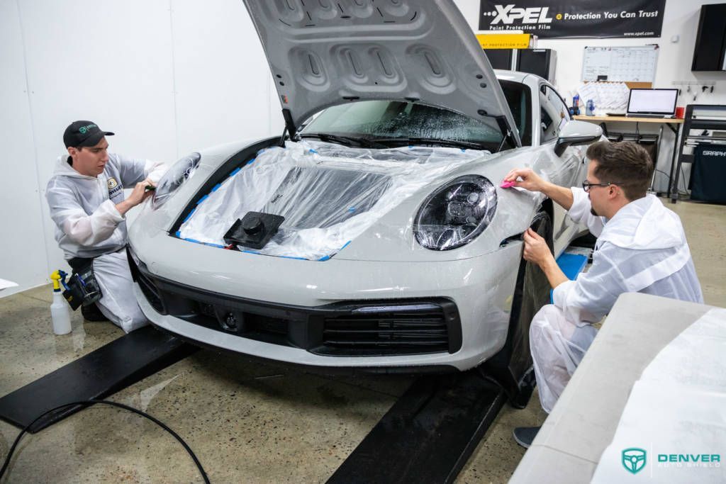 Two men are wrapping a white porsche 911 with a protective film.