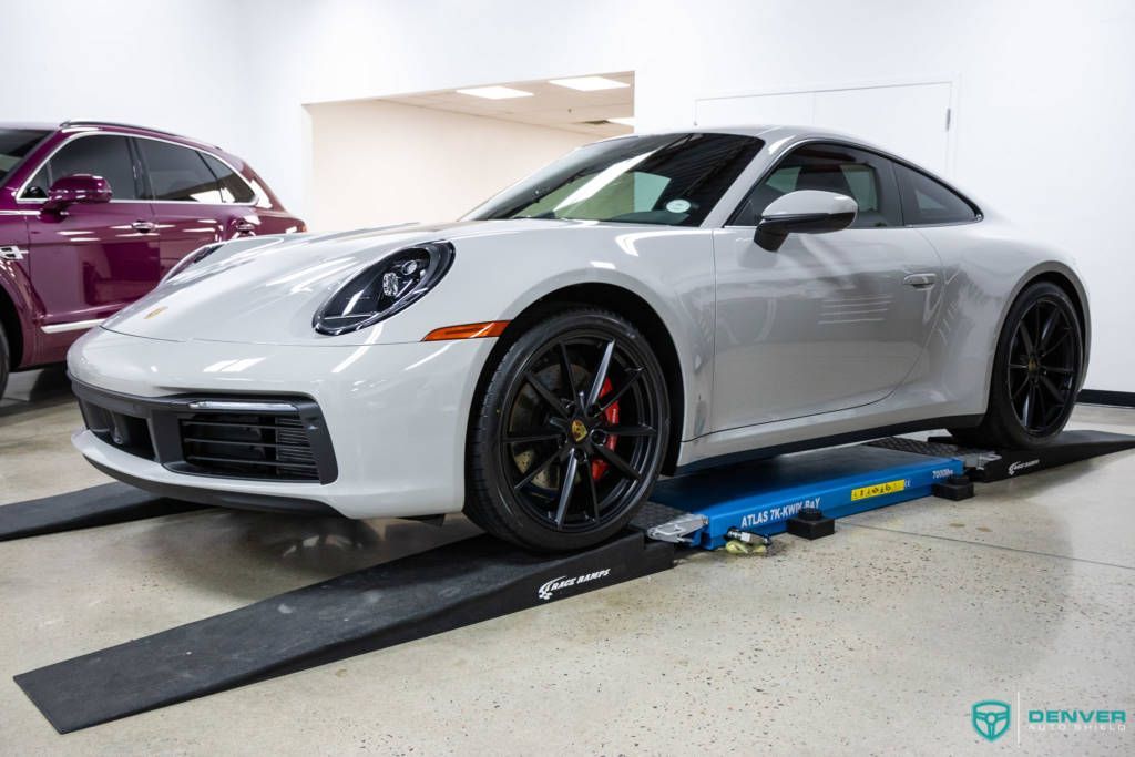 A white porsche 911 is parked on a ramp in a garage.