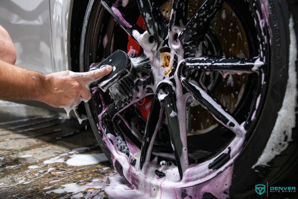 A person is washing a car wheel with soap and a brush.