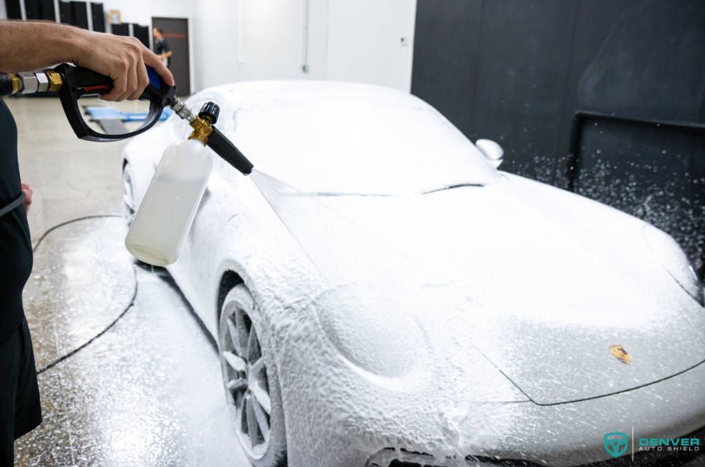 A man is washing a white sports car with foam.