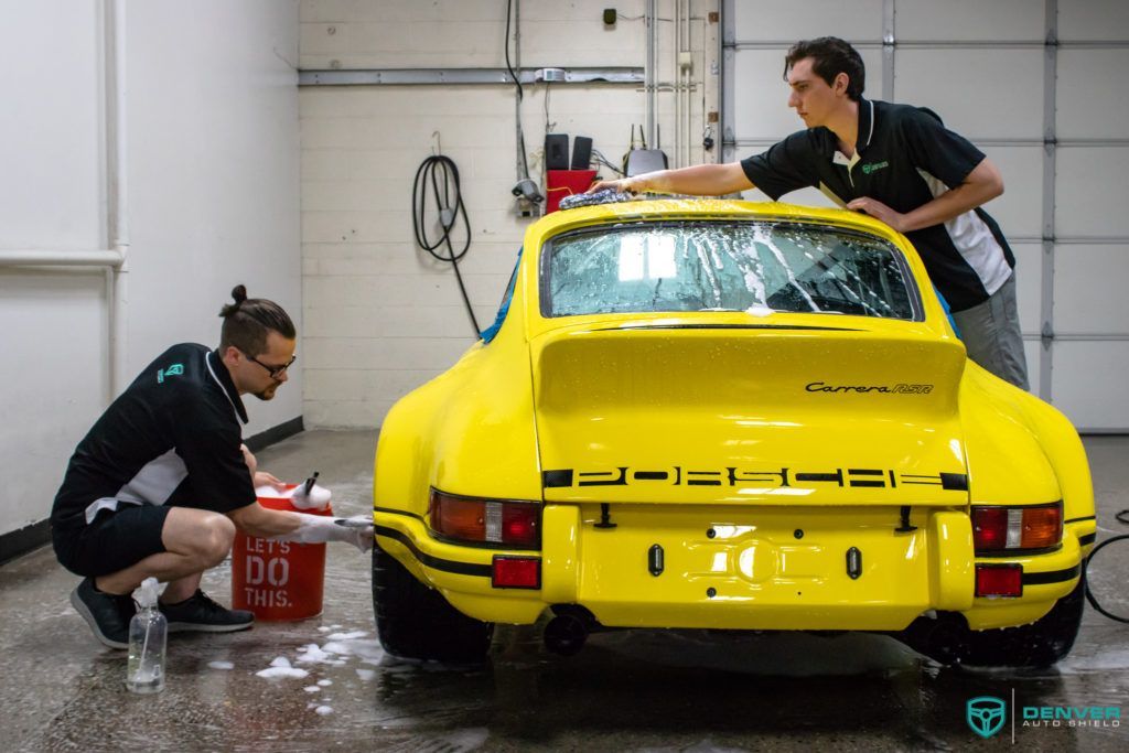 Two men are washing a yellow porsche in a garage.